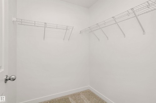 Walk-in closet featuring light beige carpeting, white wire shelving, and crisp white walls - 9552 Carson Bend Bend, Edmonton, AB - Indoor With Storage