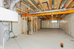 Unfinished lower level featuring exposed ceiling joists, concrete flooring, and a water heater - 