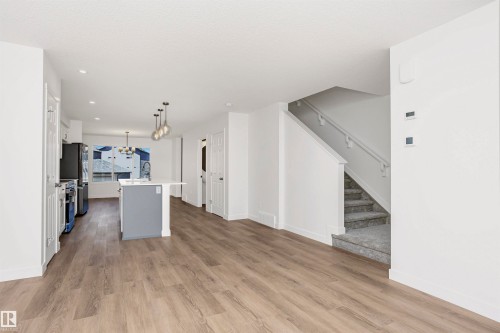 Spacious open-concept living area featuring wood-finish flooring, a kitchen island with seating, pendant lighting, and a staircase with carpeting and a handrail - 9552 Carson Bend Bend, Edmonton, AB - Indoor