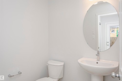 Bathroom featuring a pedestal sink with a chrome faucet, oval mirror, and white toilet - 9564 Carson Bend Bend, Edmonton, AB - Indoor Photo Showing Bathroom