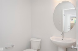 Bathroom featuring a pedestal sink with a chrome faucet, oval mirror, and white toilet - 