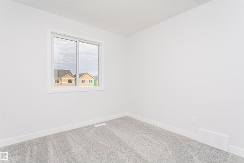 Bright interior space featuring a window with white trim, light gray patterned carpeting, white baseboards, and neutral wall tones - 9564 Carson Bend Bend, Edmonton, AB - Indoor Photo Showing Other Room