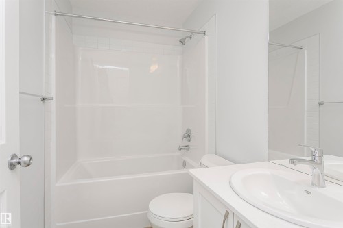Bathroom featuring a bright white tub and shower combination with chrome fixtures, a white vanity with an integrated sink, a large mirror, and a modern toilet - 9564 Carson Bend Bend, Edmonton, AB - Indoor Photo Showing Bathroom