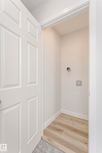 Laundry area featuring wood-finish flooring, white baseboards, and a white six-panel door - 9564 Carson Bend Bend, Edmonton, AB - Indoor Photo Showing Other Room