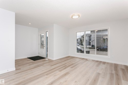 Bright interior space featuring a light wood-finish flooring, white walls, and a large front-facing window - 9564 Carson Bend Bend, Edmonton, AB - Indoor