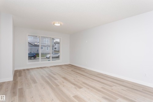 Spacious room featuring wood-finish flooring, white baseboards, and a large multi-pane window - 9564 Carson Bend Bend, Edmonton, AB - Indoor