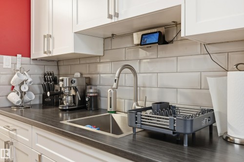 Kitchen featuring white shaker-style cabinetry, a dark countertop, subway tile backsplash, and a stainless steel sink with a gooseneck faucet - 105 7204 81 Avenue, Edmonton, AB - Indoor Photo Showing Kitchen