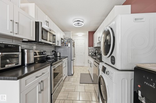 Galley kitchen with white shaker cabinetry, dark countertops, stainless steel appliances, and subway tile backsplash - 105 7204 81 Avenue, Edmonton, AB - Indoor Photo Showing Laundry Room