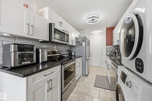 Galley kitchen featuring white shaker-style cabinetry, dark countertops, and a subway tile backsplash - 105 7204 81 Avenue, Edmonton, AB - Indoor