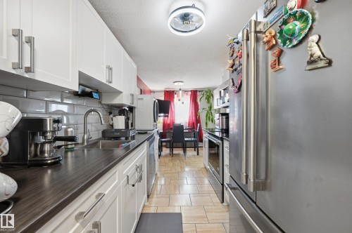 Galley kitchen featuring white cabinetry, wood-finish countertops, stainless steel appliances, and a subway tile backsplash - 105 7204 81 Avenue, Edmonton, AB - Indoor Photo Showing Kitchen With Double Sink