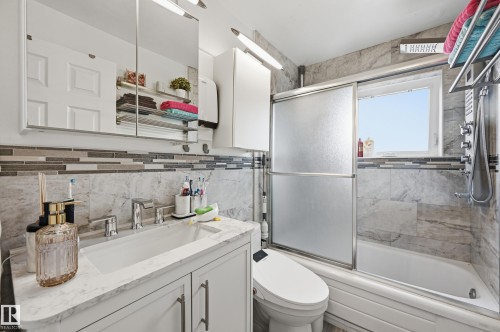 Bathroom featuring a vanity with a white countertop and undermount sink, a tiled backsplash, and a bathtub with a sliding glass door - 105 7204 81 Avenue, Edmonton, AB - Indoor Photo Showing Bathroom