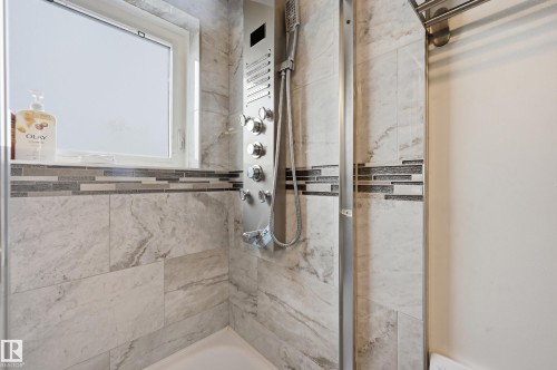 Shower stall with large format grey-toned wall tiles, a decorative mosaic tile accent band, and a multi-function shower panel - 105 7204 81 Avenue, Edmonton, AB - Indoor Photo Showing Bathroom