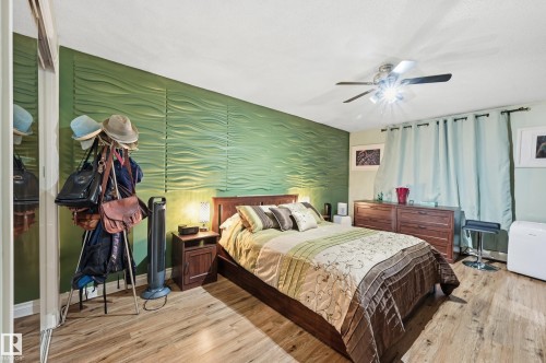Room featuring an accent wall with a wave-patterned textured finish, wood-finish flooring, and a ceiling fan with integrated lighting - 105 7204 81 Avenue, Edmonton, AB - Indoor Photo Showing Bedroom