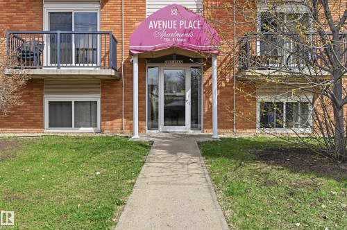 Brick exterior building featuring a covered entrance with a glass door, concrete walkway, and ground-level windows - 105 7204 81 Avenue, Edmonton, AB - Outdoor