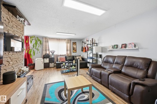 Living area featuring wood-finish flooring, a stone-accented wall, white walls, and recessed lighting - 105 7204 81 Avenue, Edmonton, AB - Indoor Photo Showing Living Room