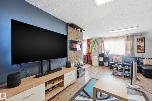 Spacious living area featuring wood-finish flooring, a textured accent wall, and recessed ceiling lighting - 105 7204 81 Avenue, Edmonton, AB - Indoor