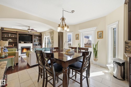 Dining area featuring a bronze chandelier, light tile flooring, and multiple windows with decorative trim - 3105 65 Street, Beaumont, AB - Indoor Photo Showing Dining Room With Fireplace