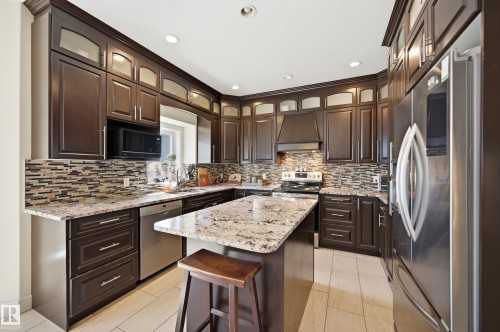 Kitchen featuring rich wood cabinetry, stainless steel appliances, a mosaic tile backsplash, light granite countertops, and recessed lighting - 3105 65 Street, Beaumont, AB - Indoor Photo Showing Kitchen With Upgraded Kitchen