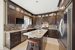 Kitchen featuring rich wood cabinetry, stainless steel appliances, a mosaic tile backsplash, light granite countertops, and recessed lighting - 