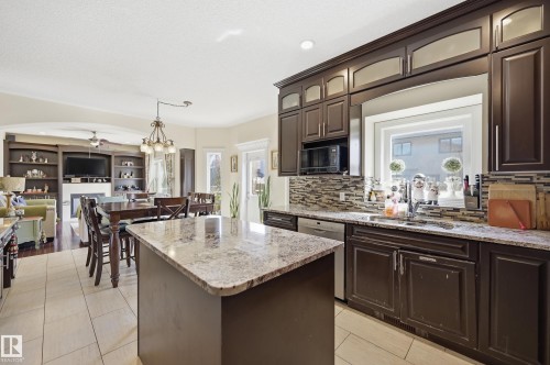 Kitchen featuring dark wood cabinetry, granite countertops, tile backsplash, and a large window above the sink - 3105 65 Street, Beaumont, AB - Indoor Photo Showing Kitchen With Double Sink With Upgraded Kitchen