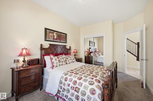 Bedroom featuring neutral wall paint, carpet flooring, a mirrored closet, and an open doorway revealing a staircase with dark wood newel posts and railings - 3105 65 Street, Beaumont, AB - Indoor Photo Showing Bedroom
