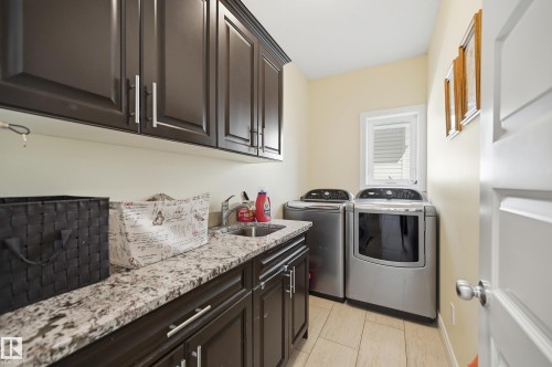 Dedicated laundry room featuring dark wood-finish cabinetry, a stone-finish countertop with an undermount sink, and light-toned tile flooring - 3105 65 Street, Beaumont, AB - Indoor Photo Showing Laundry Room