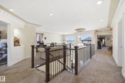 Upper-level landing featuring plush carpet flooring, decorative crown molding, recessed lighting, and dark wood railings with wrought iron spindles overlooking a lower level - 