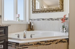 Corner soaking tub with polished chrome fixtures, surrounded by neutral-toned tile with a decorative glass mosaic accent - 