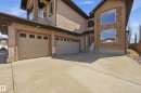 Stucco exterior with stone accents, featuring a prominent front entrance with double oval-paneled doors, a three-car garage, and an upper-level balcony with glass railings - 3105 65 Street, Beaumont, AB  - Outdoor With Exterior 