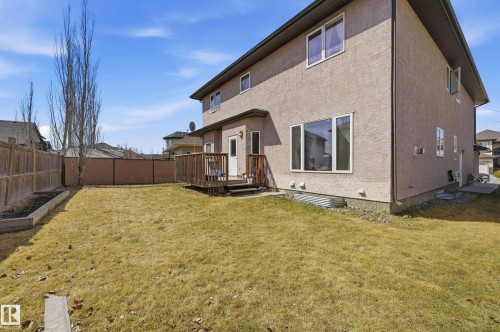 Rear exterior featuring a wood deck, stucco siding, multiple windows, and a fully fenced yard with raised garden beds - 3105 65 Street, Beaumont, AB - Outdoor With Exterior
