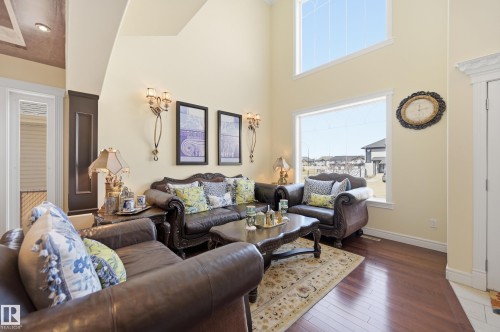 Spacious living area featuring high ceilings, large windows, wood-finish flooring, and decorative wall sconces - 3105 65 Street, Beaumont, AB - Indoor Photo Showing Living Room