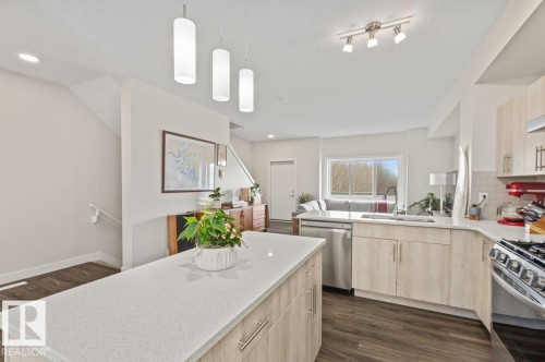 Open-concept kitchen featuring light-toned cabinetry, stainless steel appliances, a center island with a light-colored countertop, and recessed and pendant lighting - 21 979 Crystallina Nera Way, Edmonton, AB - Indoor Photo Showing Kitchen With Double Sink