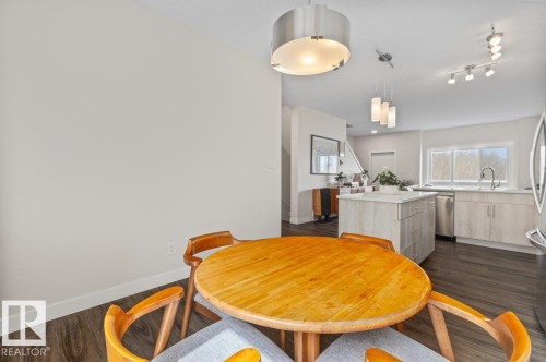 Open-concept kitchen and dining area featuring dark wood-finish flooring, light cabinetry, a kitchen island with built-in storage, stainless steel appliances, and multiple lighting fixtures - 21 979 Crystallina Nera Way, Edmonton, AB - Indoor Photo Showing Dining Room