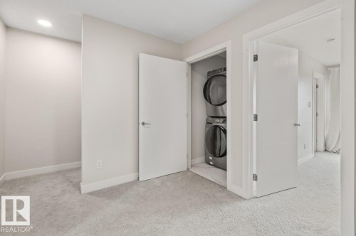 Laundry closet with stackable washer and dryer, featuring light grey carpeting, white trim, and a recessed ceiling light - 21 979 Crystallina Nera Way, Edmonton, AB - Indoor Photo Showing Laundry Room