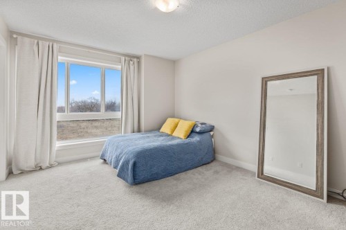 Room featuring large windows with white trim, light-colored carpeting, neutral wall paint, and a textured ceiling - 21 979 Crystallina Nera Way, Edmonton, AB - Indoor Photo Showing Bedroom