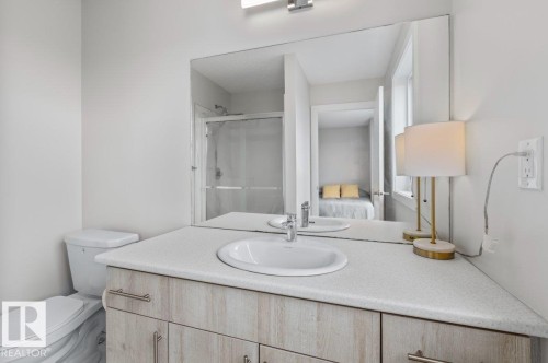 Bathroom featuring a light-toned vanity with an integrated sink, a large wall-mounted mirror, and a toilet - 21 979 Crystallina Nera Way, Edmonton, AB - Indoor Photo Showing Bathroom