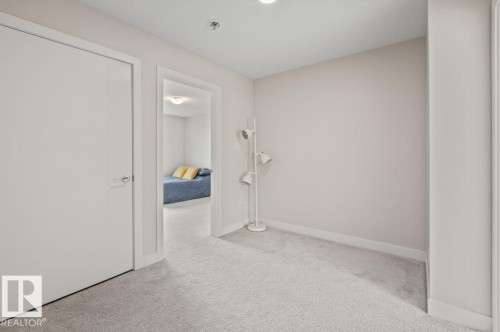 Carpeted hallway featuring a closed white door and an open doorway revealing an interior room - 21 979 Crystallina Nera Way, Edmonton, AB - Indoor Photo Showing Other Room