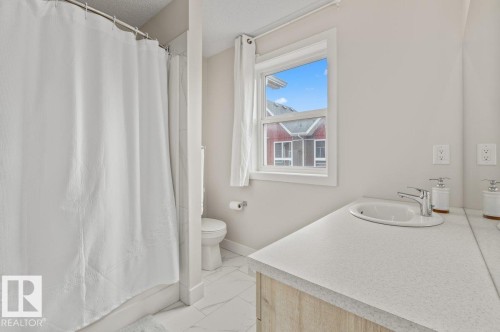 Bathroom featuring a light wood-finish vanity with an undermount sink, a light-toned countertop, and chrome fixtures - 21 979 Crystallina Nera Way, Edmonton, AB - Indoor Photo Showing Bathroom