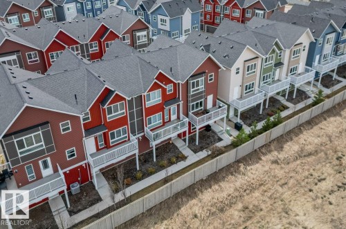 Rows of multi-story townhomes with varying exterior colors, gray shingle roofs, balconies with white railings, and individual ground-level patios - 21 979 Crystallina Nera Way, Edmonton, AB -  With Facade