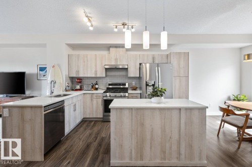 Contemporary kitchen featuring wood-finish cabinetry, stainless steel appliances, a subway tile backsplash, white countertops, and a central island with pendant lighting - 21 979 Crystallina Nera Way, Edmonton, AB - Indoor Photo Showing Kitchen With Upgraded Kitchen
