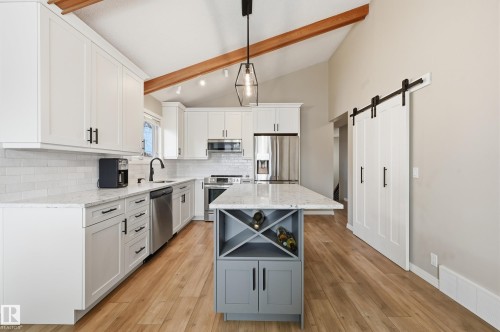 Vaulted ceiling kitchen featuring exposed wood beams, white shaker cabinetry, stainless steel appliances, and a central island with integrated wine storage - 1729 65 Street, Edmonton, AB - Indoor Photo Showing Kitchen With Stainless Steel Kitchen With Upgraded Kitchen