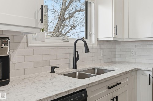 Kitchen featuring white shaker-style cabinetry, a dual-basin stainless steel sink with a matte black gooseneck faucet, light-toned countertops with subtle veining, and a white subway tile backsplash - 1729 65 Street, Edmonton, AB - Indoor Photo Showing Kitchen With Double Sink
