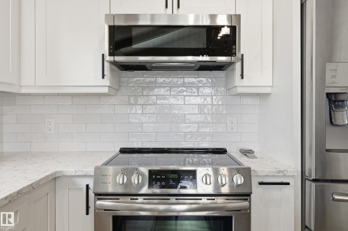 Stainless steel range with a built-in microwave, white shaker-style cabinetry, light-toned countertops, and a white subway tile backsplash - 1729 65 Street, Edmonton, AB - Indoor Photo Showing Kitchen With Stainless Steel Kitchen With Upgraded Kitchen