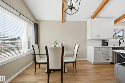 Kitchen and dining area featuring wood-finish flooring, exposed wood ceiling beams, and a black geometric chandelier - 1729 65 Street, Edmonton, AB - Indoor Photo Showing Other Room