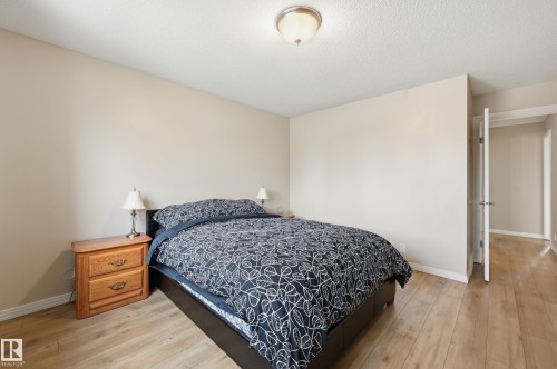 Light-toned walls complement wood-finish flooring in this room featuring a ceiling-mounted light fixture and white baseboards - 1729 65 Street, Edmonton, AB - Indoor Photo Showing Bedroom