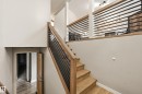 Hardwood staircase with modern metal railing, wood-finish flooring, white painted walls, and an upper-level loft area featuring a white brick fireplace with a dark mantel - 1729 65 Street, Edmonton, AB  - Indoor Photo Showing Other Room 