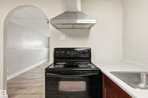 Compact kitchen area featuring a black electric range with an overhead stainless steel range hood, white countertops, and a stainless steel sink - 1729 65 Street, Edmonton, AB - Indoor