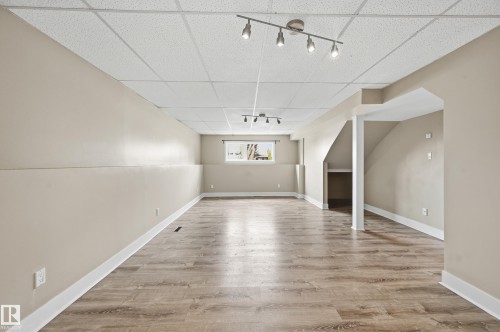 Expansive lower-level room featuring wood-finish flooring, neutral wall tones, white trim, and a drop ceiling with track lighting - 1729 65 Street, Edmonton, AB - Indoor Photo Showing Other Room