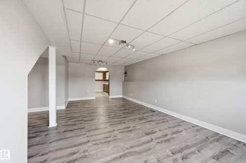 Spacious finished basement featuring wood-finish flooring, light gray walls, white trim, and a drop ceiling with integrated track lighting - 1729 65 Street, Edmonton, AB - Indoor Photo Showing Other Room