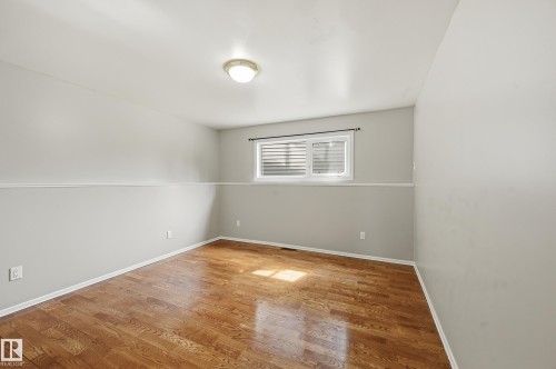 Spacious room featuring wood-finish flooring, light gray walls with white wainscoting, a flush-mount ceiling light, and a horizontal window with white blinds - 1729 65 Street, Edmonton, AB - Indoor Photo Showing Other Room